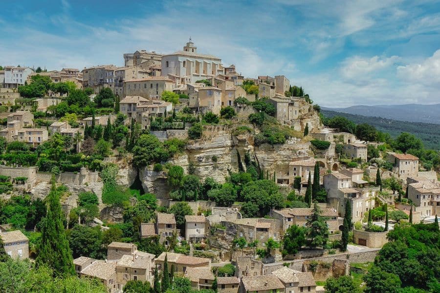 Hilltop village of Gordes in Provence, with stone houses cascading down the rocky hillside, surrounded by lush greenery – the kind of dreamy setting featured in movies that will make you want to move to France.