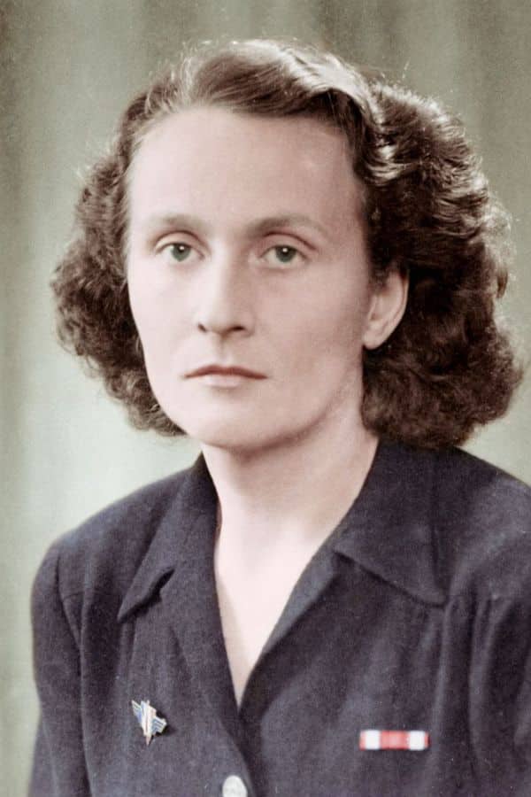Formal portrait of Catherine Dior in a navy suit, wearing a Resistance medal and French military decoration. Her solemn expression reflects her role in the French Resistance during WWII.